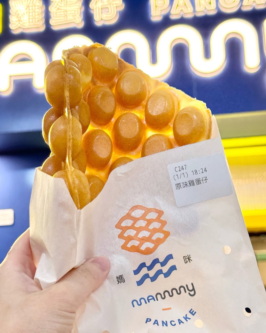 Hong Kong egg waffle held up in front of a neon stall sign
