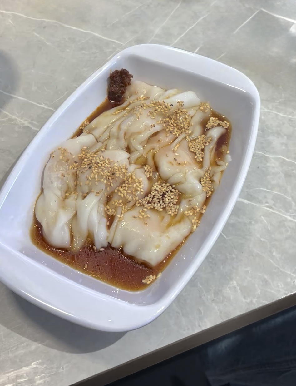Cheung fun rice rolls in a white dish with sesame seeds and sauce